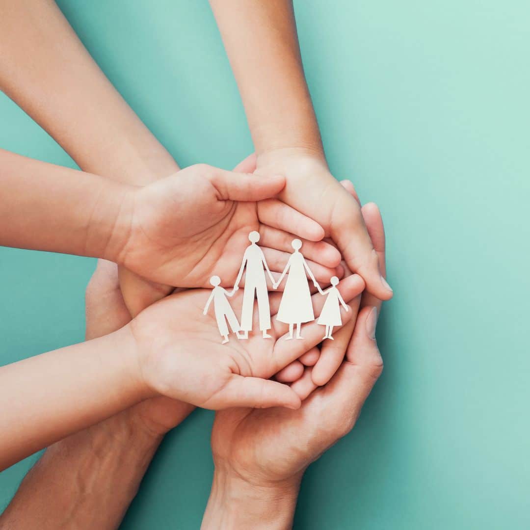 hands craddling a paper cutout of a family