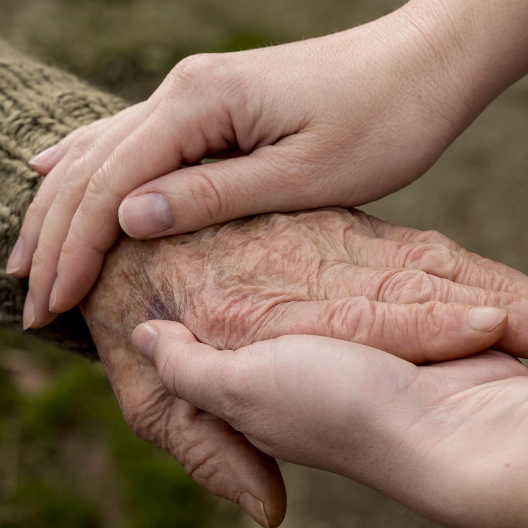A young person holding hands with an elderly person
