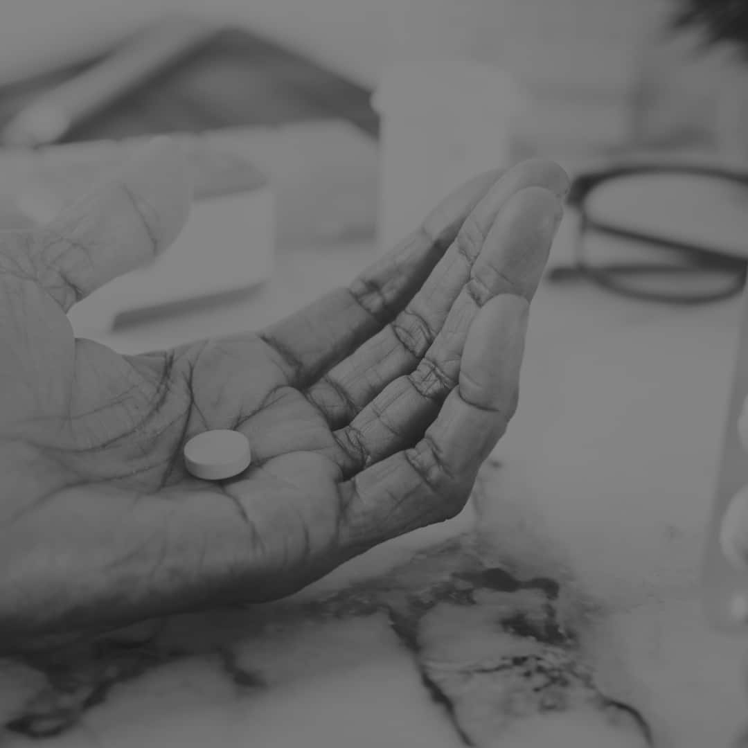 Black and white photo of a pill in the palm of a wrinkly hand