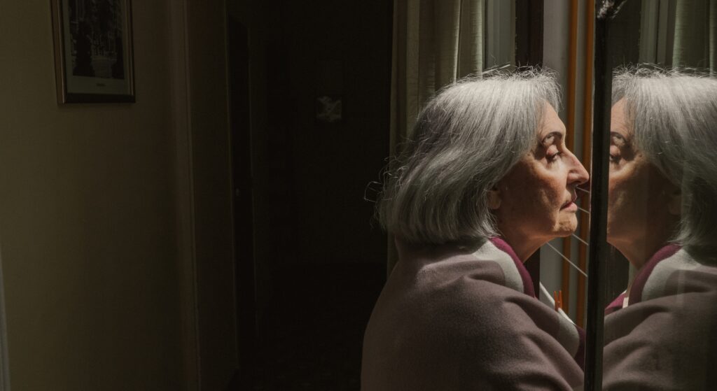 Senior woman looking in the mirror|Black and white image of someone holding their wrist to stop tremors|Senior woman screaming in their sleep|Black and white photo of a pill in the palm of a wrinkly hand|Woman holding her legs while sitting at the edge of her bed
