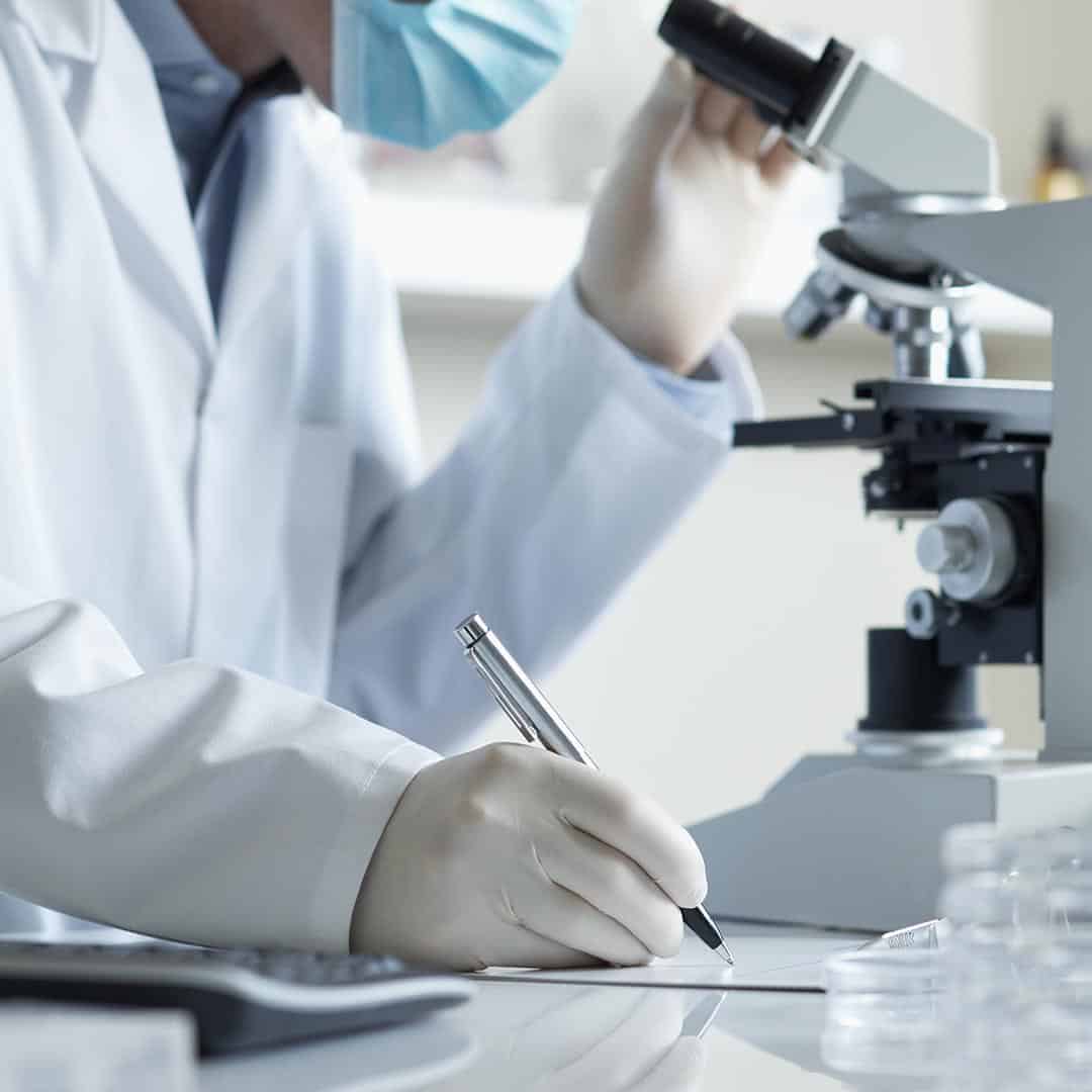 Scientist looking through a microscope and writing notes down