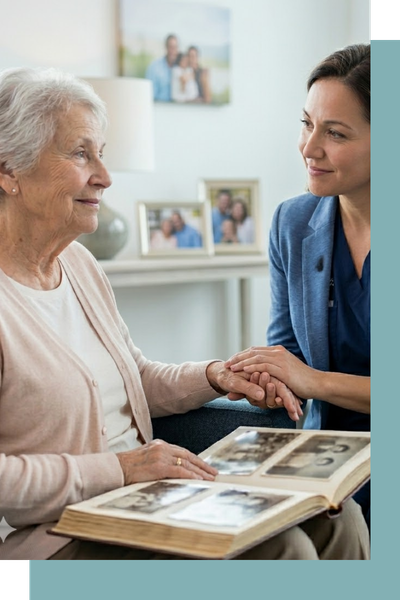 A candid photograph of a memory care specialist gently holding the hand of an elderly woman as they look at an old photo album together in a supportive environment.